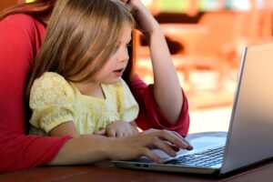 child sat in parent's lap using a laptop together