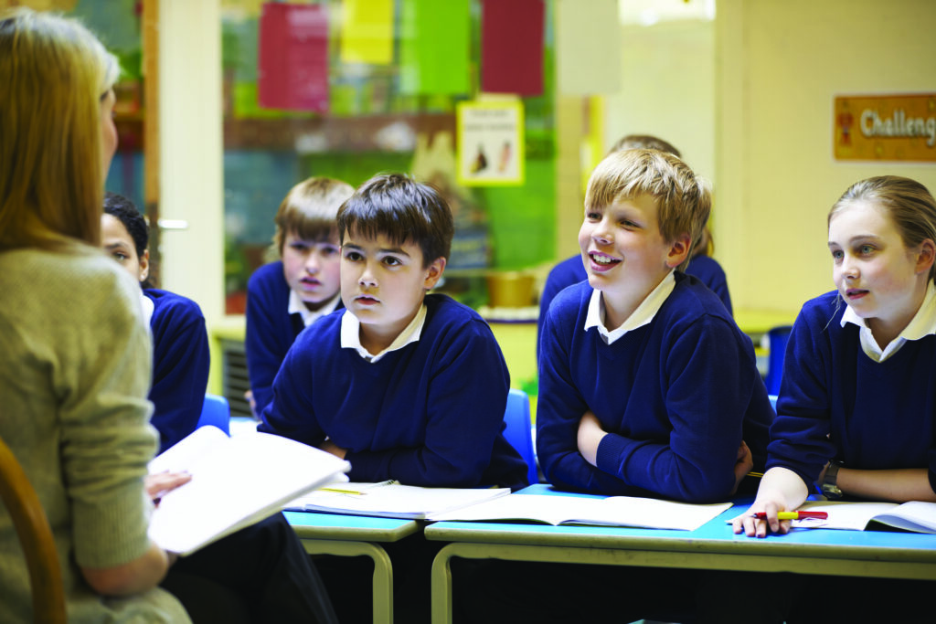 Teacher communicating with three engaged-looking children in blue uniforms.